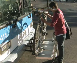 A person loads their bicycle onto a Roseville Transit bus bike rack.